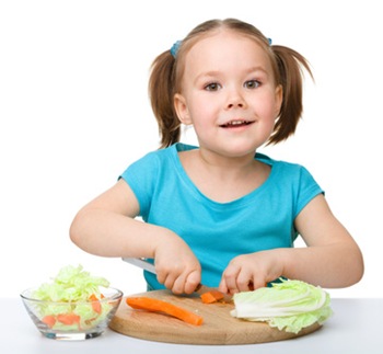 Little girl is cutting carrot for salad